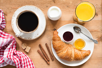 Breakfast table with croissant, coffee, orange juice and jam. Rustic wood table background, top view