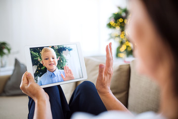 A grandmother with tablet making videocall with small grandson at Christmas time.