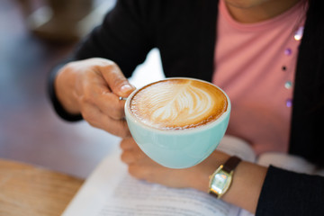 Women reading a book and eating Latte arts coffe hot coffee on wooden table.barista art concept.