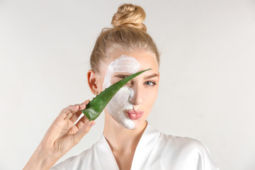 Beautiful young woman with facial mask containing aloe vera extract, on light background - obrazy, fototapety, plakaty