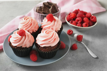 Plate with tasty cupcakes and raspberry on grey table