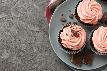 Plate with sweet cupcakes and chocolate on grey table