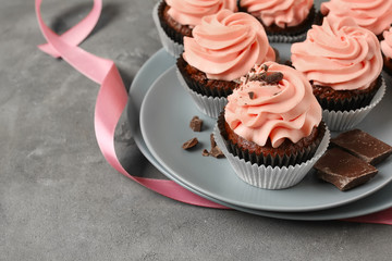 Plate with sweet cupcakes and chocolate on grey table