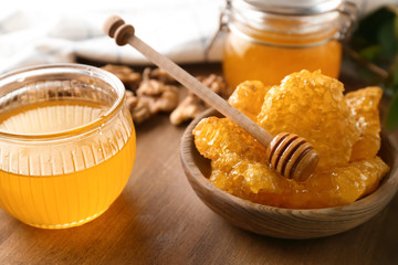 Fototapeta premium Bowl with honeycomb, jar of honey and dipper on table