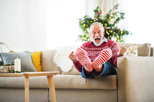 A cheerful senior man with red and white socks at home at Christmas time, having fun.