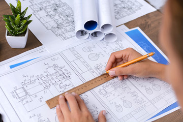 A girl (architect, student, businesswoman) works (draws, counts) at a table with business accessories (laptop, smartphone, pens, magnifier), accessories for drawing (plans, rulers) and training