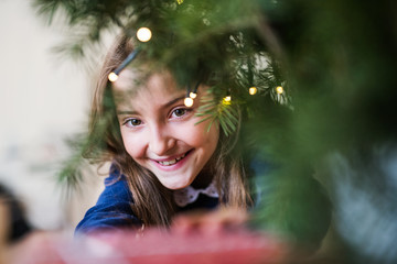 A close-up of small girl standing by a Christmas tree at home. Copy space.