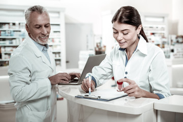 Obraz premium Work in drugstore. Dark-haired beaming experienced woman working in drugstore feeling busy receiving new medicine
