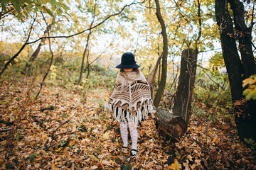 Outdoor portrait of a cute little girl in an autumn forest, wearing knitted poncho and hat. Autumn mood in the forest. Atmospheric walk through the forest of a beautiful girl