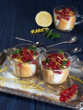Three glass cups of limoncello (or limoncino) tiramisu topped with redcurrants and mint leaves, on a silver tray set on a dark background