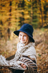 Outdoor portrait of a cute little girl in an autumn forest, wearing knitted poncho and hat. Autumn mood in the forest. Atmospheric walk through the forest of a beautiful girl