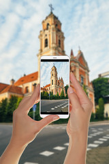 Naklejka premium A tourist is taking a photo of View old church in the center of Vilnius, Lithuania on a mobile phone