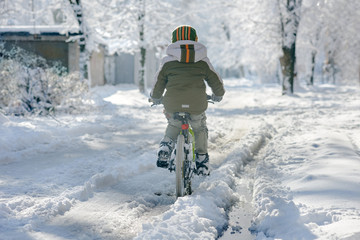 Back view of little boy riding bike in city on winter