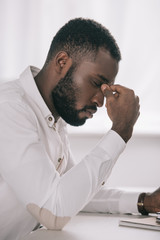 side view of tired african american businessman touching nose bridge in office