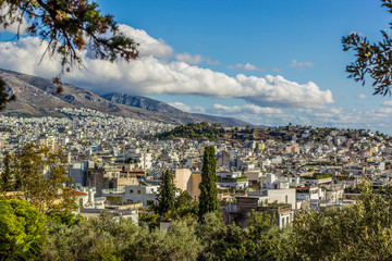 Fototapeta na wymiar Athens city view of capital of Greece from hill top and foreshortening between trees branches to many buildings, mountain and blue sky with clouds