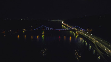 Fototapeta na wymiar Aerial view from Drone: Top view of the night promenade with bridges and cars. Driving with headlights on the road.