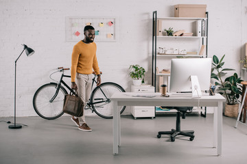 handsome african american designer in orange sweater entering office with briefcase