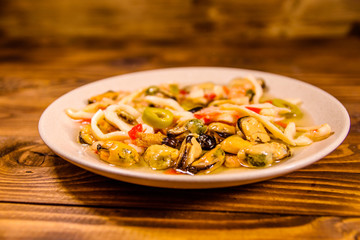 Ceramic plate with different sea food and olives on wooden table