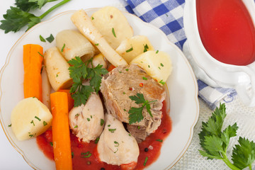 Boiled beef and chicken meat with creamy tomato sauce served with vegetables on white plate, top view