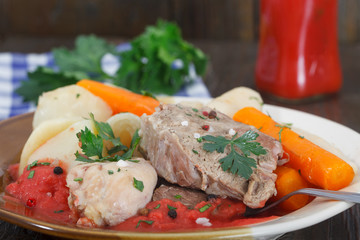 Boiled beef and chicken meat with creamy tomato sauce served with potatoes, carrots, dill and celery. Homemade cuisine, wooden background.