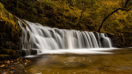 Waterfall Ddwli Isaf near pontneddfechan in the brecon beacons national park, Wales. It is autumn, and golden leaves are all around.  Long shutter speed for a smooth effect on the water