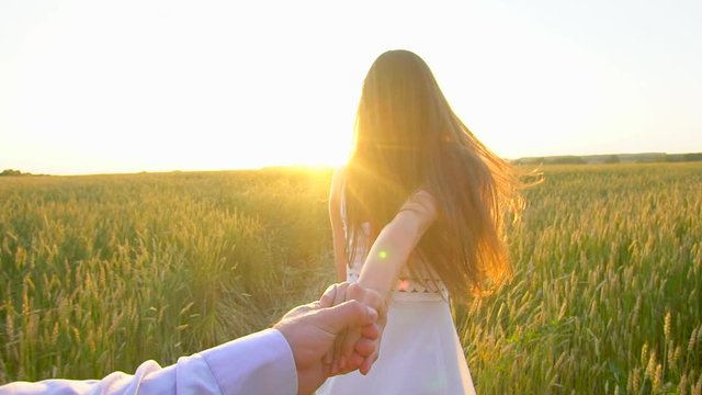 Follow me. Happy couple holding hands, running on golden wheat field and having fun outdoors. Couple walking on meadow. Young Man and beautiful woman, happy family in love. Sun flare. Slow motion