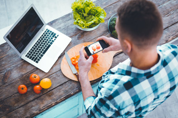 Professional photography. Nice young man holding his modern smartphone while taking photos of food