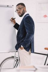 bearded african american businessman in velvet jacket writing on whiteboard in office with bicycle