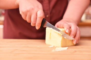 Female hands and knife cut fresh parmesan cheese on a cutting board. Close-up