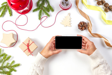 Christmas planing, online shopping concept. Woman hands with mobile phone, christmas presents, decorations on white background