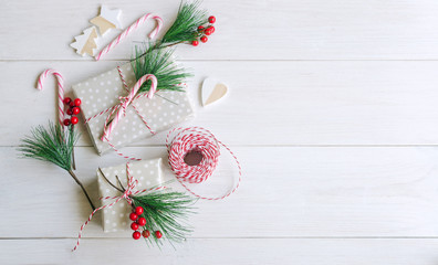 Christmas packaging background. Different wrap presents, fir tree branch with red berries, wrapping paper, roll of red and white thread and christmas candies. Merry Xmas concept.Top view