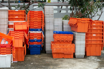 Stacked of old plastic basket and boxes in orange, blue and white color on concrete floor with tree and concrete fence in background