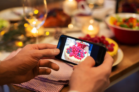food, technology and holidays concept - close up of male hands photographing cake by smartphone at christmas dinner