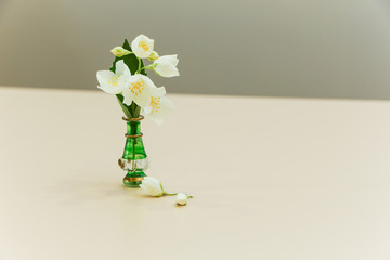 Jasmine flowers in a little green vase on a wooden background.
