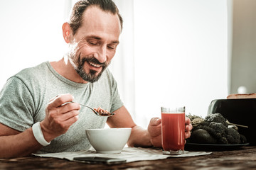 So tasty. Delighted positive man smiling while having his breakfast