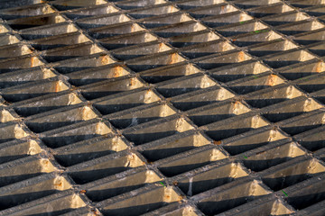 Old metal drain host cover plate textured with sunlight and shadow. Background for pattern and texture design