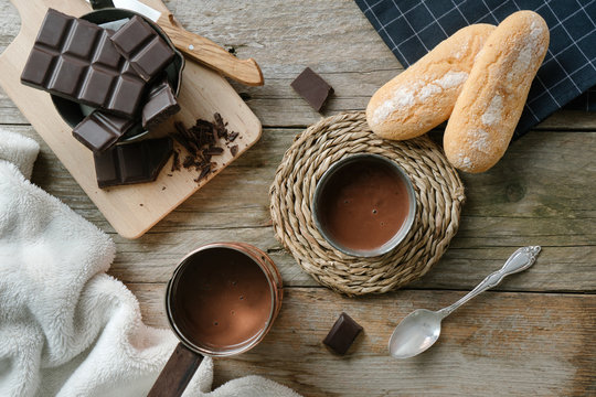 Top view of a hot chocolate cup, a cooper pot with hot chocolate and a cutting board with chocolate chunks