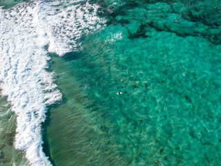 Fototapeta na wymiar Vista aerea di un mare cristallino con onde e surfisti. Onde che si infrangono sulla spiaggia al tramonto, controluce. Playa De La Canteria. Oceano Atlantico. Orzola, Lanzarote, Isole Canarie. Spagna