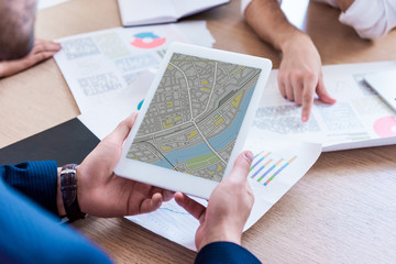 partial view of businessman with tablet with map on screen during meeting in office
