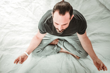Peace of mind. Top view of a nice handsome man meditating while sitting on his bed