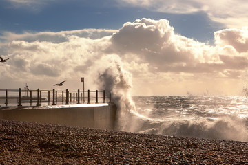 Fototapeta na wymiar Spectactular Sea, stormy waves hitting harbour arm or jetty, clouds clearing to let sunlight through