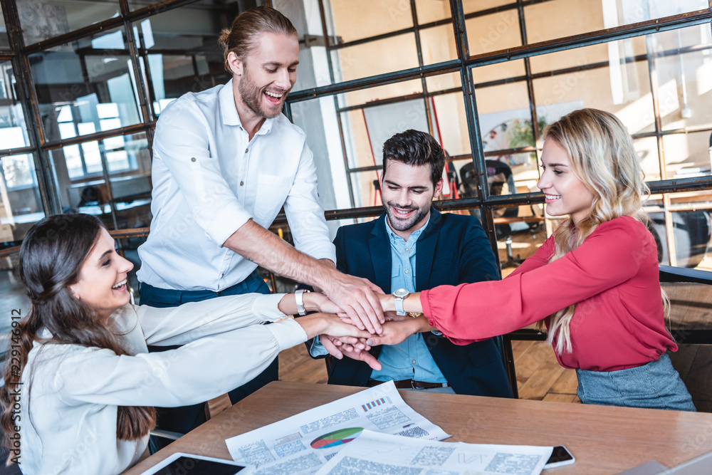 Wall mural happy business team holding hands at workplace in office