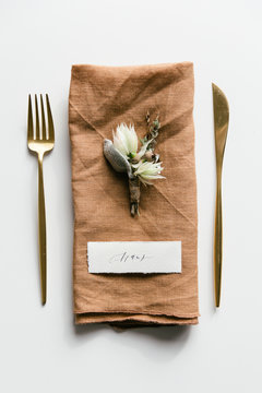 Table setting with golden colored cutlery styled with a orange linnen napkin, boutonniere and handwritten place card.