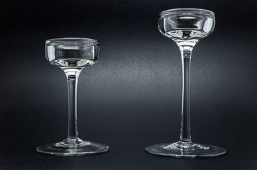 Two glass candlesticks standing on a black, shiny background.