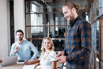 smiling young businessman using digital tablet and colleagues working behind in office