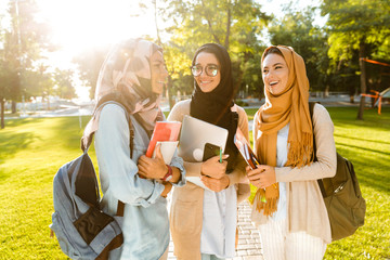 Happy friends muslim sisters women walking outdoors holding books.