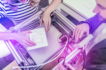 Using printer. Top view of two modern businessmen feeling cheerful while using 3D printer while working together