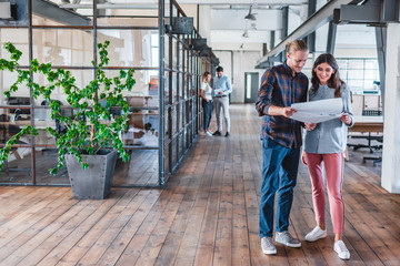 Fototapeta premium smiling young business colleagues looking at papers while standing together at workspace