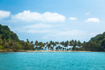 Palm trees on the sandy shore in the turquoise tropical sea against the blue sky and clouds. Beautiful seascape with a thin strip of land between the two Islands in Thailand.
