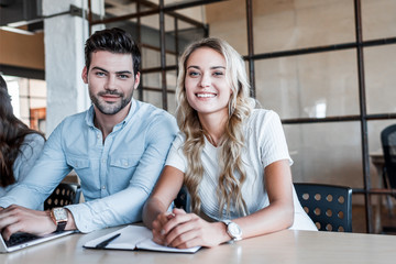 Fototapeta premium happy young business colleagues sitting together and smiling at camera in office